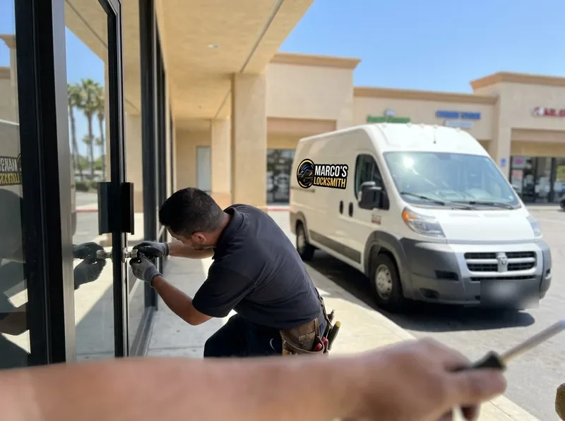 Technician servicing the lock on a glass storefront door with the Marco's Locksmith van at the curb